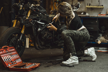 Plakat beautiful girl with long hair in the garage repairing a motorcycle