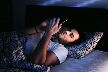 Young man using smartphone in bed at night