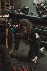 Plakat beautiful girl with long hair in the garage repairing a motorcycle
