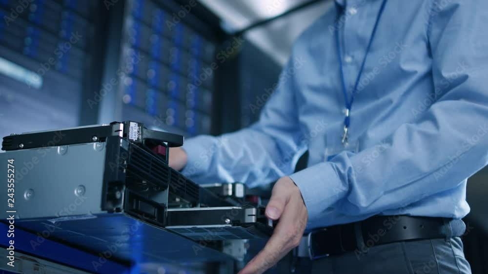 Poster In the Data Center: IT Engineer Installs New HDD Hard Drive and Other Hardware into Server Rack Equipment. IT Specialist Doing Maintenance, Running Diagnostics and Updating Hardware. Low Angle.