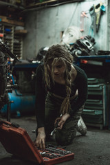 Plakat beautiful girl with long hair in the garage repairing a motorcycle