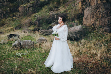 Beautiful bride in a lace dress stands on the background of stones and rocks. Wedding photography....