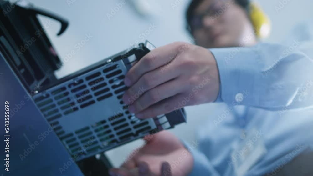 Poster In the Data Center: IT Engineer Installs New HDD Hard Drive and Other Hardware into Server Rack Equipment. IT Specialist Doing Maintenance, Running Diagnostics and Updating Hardware. Low Angle.