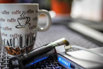Electronic cigarette connected to the power bank and cup of coffee  on table