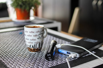 Electronic cigarette connected to the power bank and cup of coffee  on table