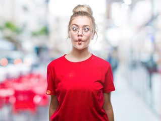Young blonde woman wearing glasses over isolated background making fish face with lips, crazy and comical gesture. Funny expression.