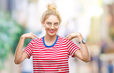 Young beautiful blonde woman wearing glasses over isolated background looking confident with smile on face, pointing oneself with fingers proud and happy.