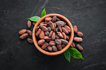 Cocoa beans in a bowl on a black background. Top view. Free copy space.
