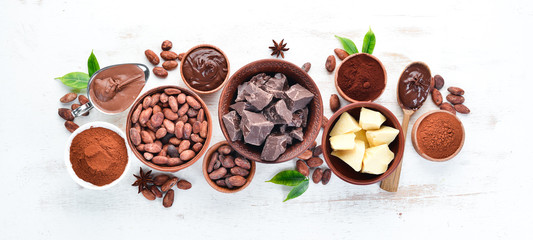 Cocoa beans, chocolate, cocoa butter and cocoa powder on a white wooden background. Top view. Free...