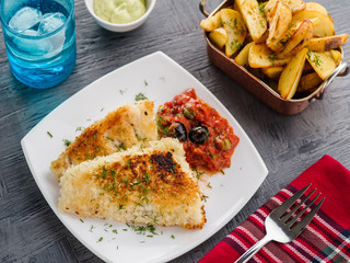Fried fish with tomato-olive sauce and potatoes.