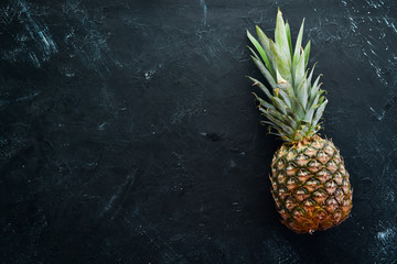 Fresh pineapple on a black stone background. Top view. Free copy space.