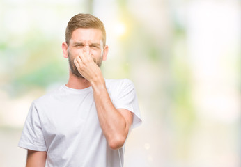 Young handsome man over isolated background smelling something stinky and disgusting, intolerable...