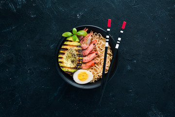 Asian food. Noodles with shrimps, avocados, eggs and chia seeds. On a black stone background. Top view. Free copy space.