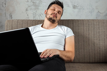 The guy in the white shirt sitting on the couch, fell asleep at work on a laptop. The concept of...