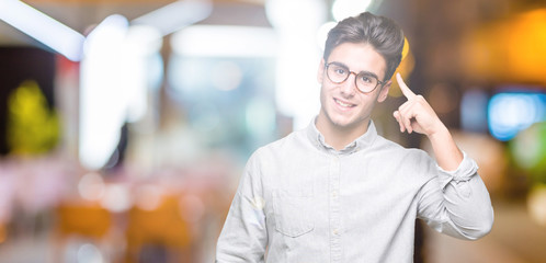 Young handsome man wearing glasses over isolated background Smiling pointing to head with one finger, great idea or thought, good memory