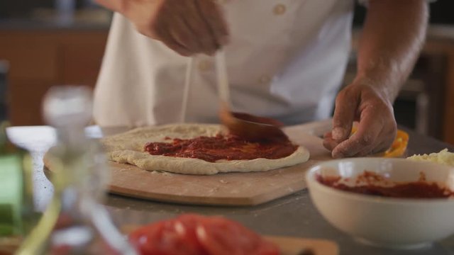 Chef spreads tomato sauce on pizza