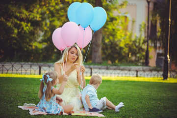 Beauty girl with colorful balloons laughing with two children. Beautiful happy young woman on a walk in the park. pastel colors