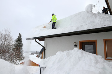 Zwei Männer schaufeln den hohen Schnee von einem Hausdach. Gefahr auf dem Hausdach im Winter durch...