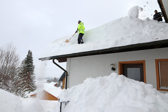 Zwei Männer schaufeln den hohen Schnee von einem Hausdach. Gefahr auf dem Hausdach im Winter durch zu schweren Schnee