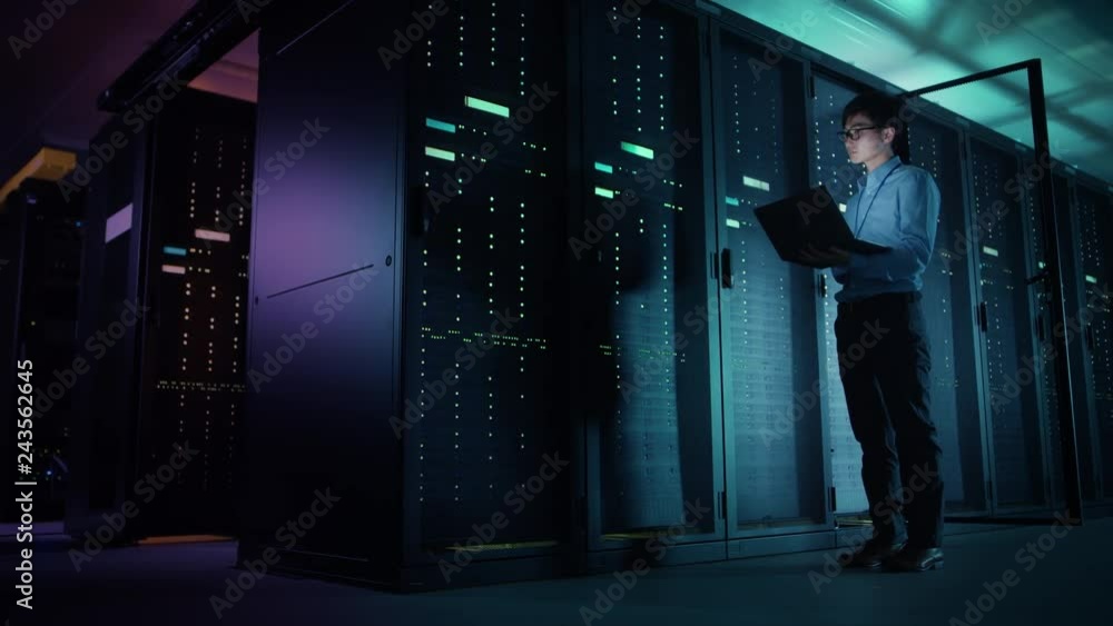 Fototapete In Data Center: Male IT Technician Running Maintenance Programme on a Laptop, Controls Operational Server Rack Optimal Functioning. Modern High-Tech Telecommunications Operational Super Computer.