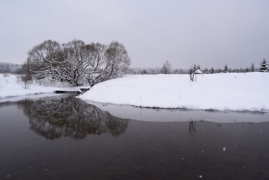 Serene Sunless Winter Landscape Minimalist Style. Dark Cold River, Grey Sky And Deep Snow