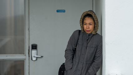 Asian woman bundeled up in parka standing next to white wall