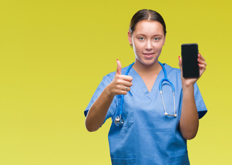 Young caucasian doctor woman showing smarpthone over isolated background happy with big smile doing ok sign, thumb up with fingers, excellent sign