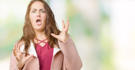 Beautiful plus size young woman wearing winter coat over isolated background crazy and mad shouting and yelling with aggressive expression and arms raised. Frustration concept.
