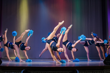 athletes perform on stage, young cheerleaders perform at the cheerleading championship, leg raised up, girl doing acrobatic and flexible tricks, girls dancer practicing mixed dance and stretching