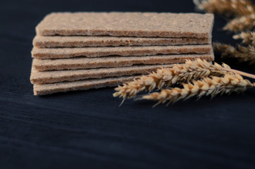 Air dietetic loaves lie on a wooden table on a dark background next to the ears of wheat