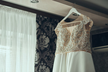 beautiful wedding dress hanging in the room, woman getting ready before  ceremony