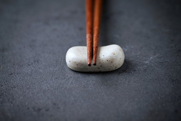Wooden chopsticks and chopstick rest on black stone background. Close up. Copy space. 
