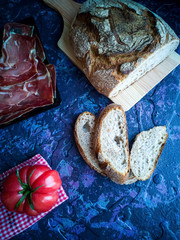 Ham, tomato, bread and herbs in composition on dark background