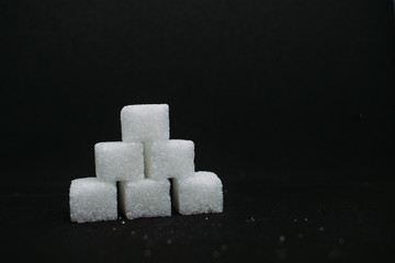Pile of sugar cubes closeup view on black dark isolated background