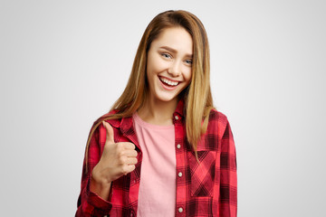 Cheerful attractive girl with long hair is defiantly laughing and showing a thumbs up sign. She...