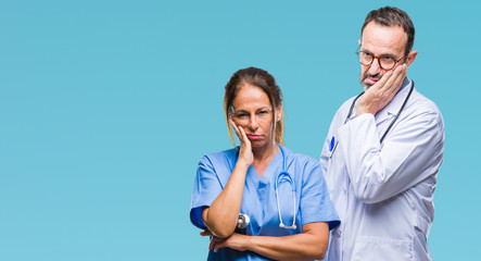 Middle age hispanic doctors partners couple wearing medical uniform over isolated background thinking looking tired and bored with depression problems with crossed arms.