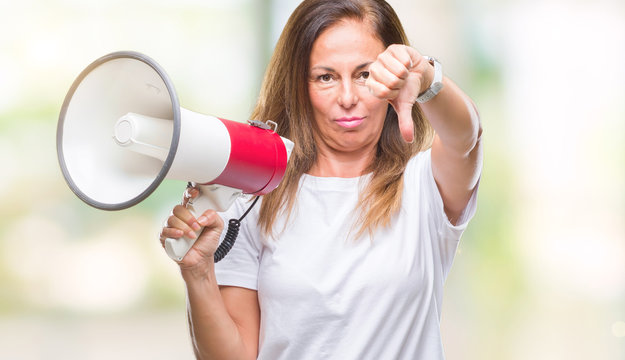 Middle age hispanic woman yelling through megaphone over isolated background with angry face, negative sign showing dislike with thumbs down, rejection concept
