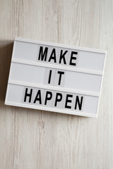 Lightbox with text 'Make it happen' on a white wooden surface, top view. From above, flat lay, overhead. Close-up.