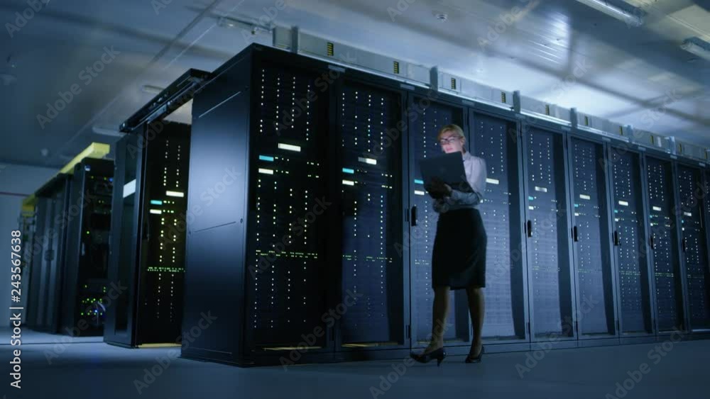 Fototapete In Data Center: Female IT Technician Walks Alongside Row of Server Racks, Uses Laptop Computer to Run Maintenance Diagnostics so that Mainframe Works at Optimal Functioning Level. 