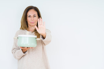 Middle age housewife woman holding iron cooking pot over isolated background with open hand doing stop sign with serious and confident expression, defense gesture