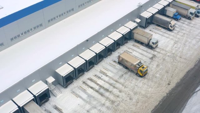 Aerial side view of a logistics loading dock with a semi-trailers trucks standing at warehouse ramp on load/unload goods