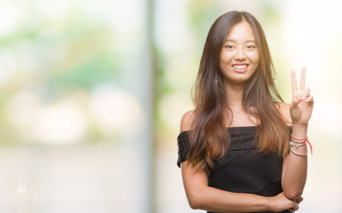 Young asian woman over isolated background smiling with happy face winking at the camera doing victory sign. Number two.