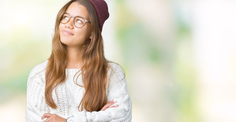 Young beautiful brunette hipster woman wearing glasses and winter hat over isolated background smiling looking side and staring away thinking.