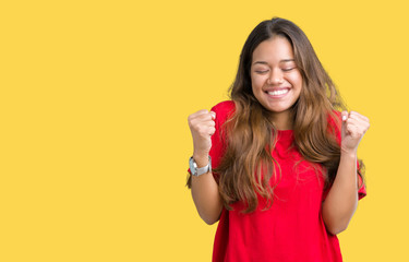 Young beautiful brunette woman wearing red t-shirt over isolated background excited for success with arms raised celebrating victory smiling. Winner concept.