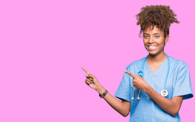 Young african american doctor woman over isolated background smiling and looking at the camera pointing with two hands and fingers to the side.
