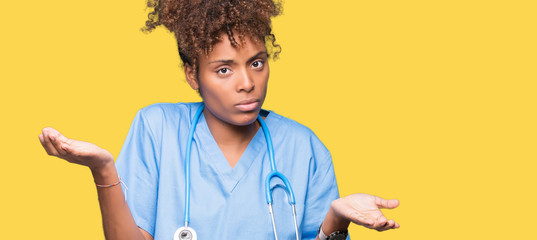 Young african american doctor woman over isolated background clueless and confused expression with arms and hands raised. Doubt concept. - obrazy, fototapety, plakaty