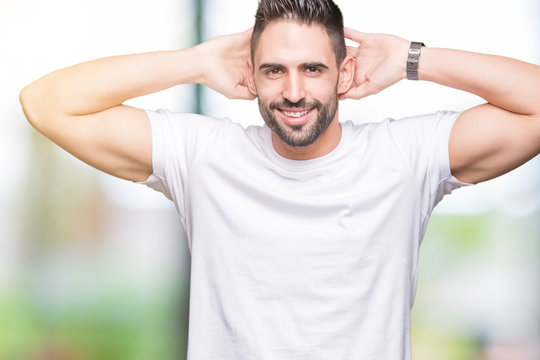 Handsome man wearing white t-shirt over outdoors background Relaxing and stretching with arms and hands behind head and neck, smiling happy