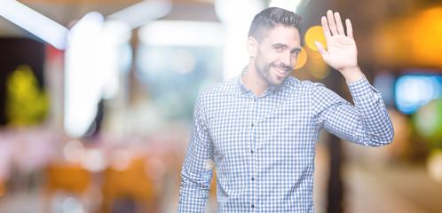 Young handsome man over isolated background Waiving saying hello happy and smiling, friendly...