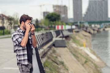 Young attractive man, a photographer, taking photographs in an urban area with an analog SLR camera