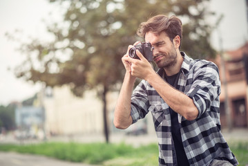 Young attractive man, a photographer, taking photographs in an urban area with an analog SLR camera